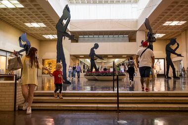 Shoppers at NorthPark Center walk by the "Five Hammering Men" series by Jonathan Borofsky....