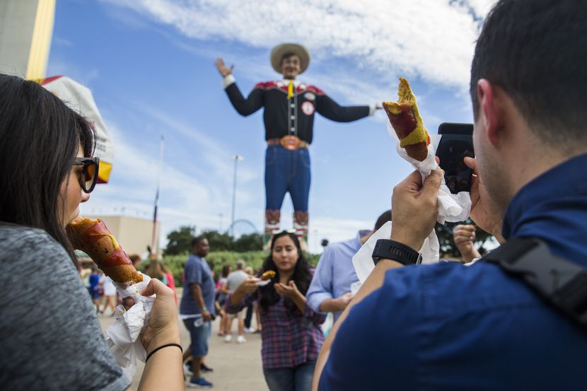 Fairgoers eat Fletcher's Corny Dogs while taking photos of Big Tex on Wednesday, October 4,...