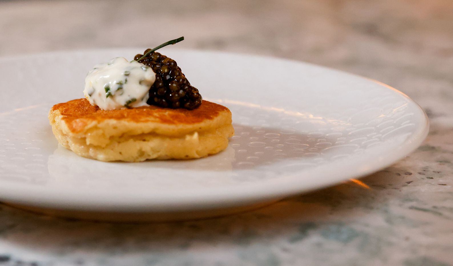A Buckwheat Potato Blini topped with Osetra Caviar and Chive Crème fraîche sits plated at...