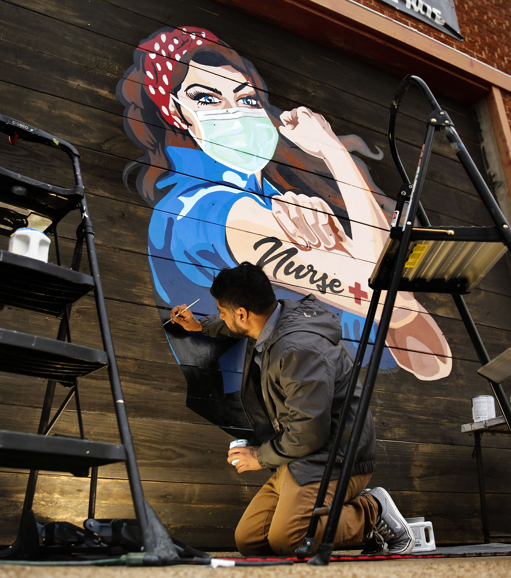 Dallas Artist Miguel Barajas paints a mural of a nurse on the exterior of Redfield's Tavern...