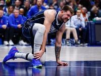 Dallas Mavericks guard Luka Doncic grabs his right foot after an awkward fall during the...
