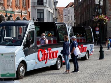 A tour operator in a protective face mask sits in an empty tour bus as he speaks with a couple on the market square of Bruges, Belgium.