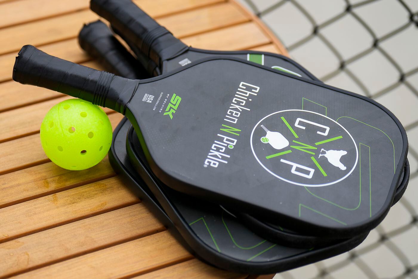 Pickleball paddles and a ball rest beside outdoor courts at Chicken N Pickle on Friday, Dec....