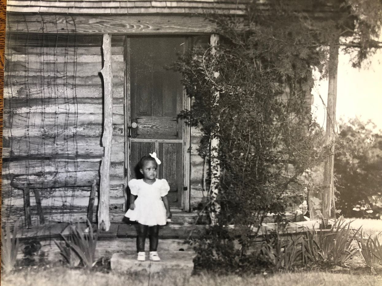 A little girl stands outside a log cabin on Miller farmland in southeast Oak Cliff in this...