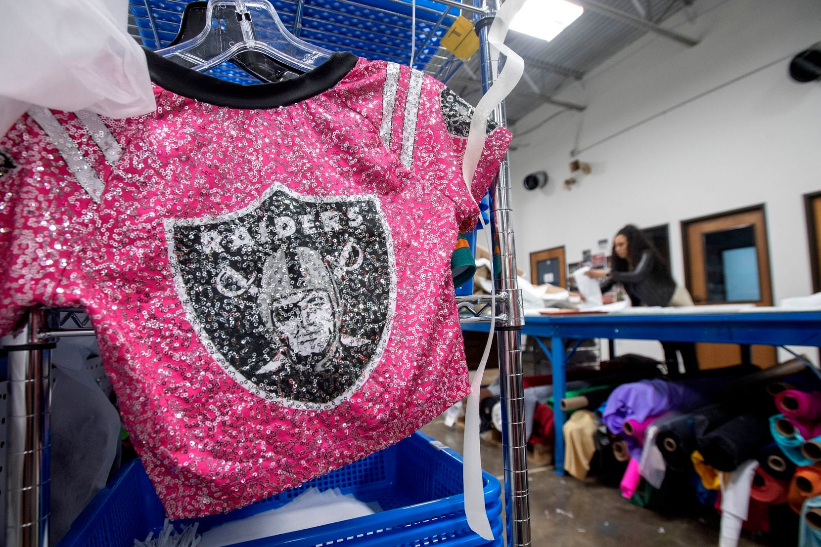 A sparkly cheerleader uniform hangs idly in the repurposed factory of Dallaswear as creative director Terra Saunders, a former Dallas Cowboys cheerleader, folds medical gowns in the background.