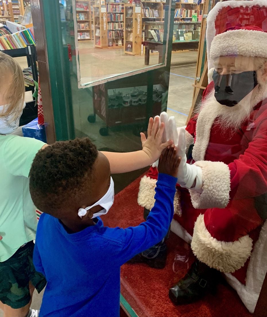 Scott Ward, the longtime Santa at Half Price Books, connects with children who came to see Santa through a protective screen at the retailer's flagship store in Dallas.