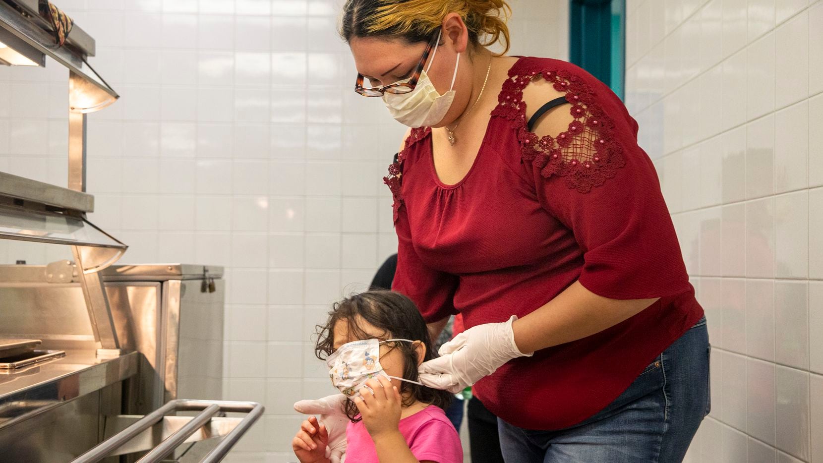 Angie Andrade refastens the face mask on her 3-year-old daughter, Abigail, as they pick up...