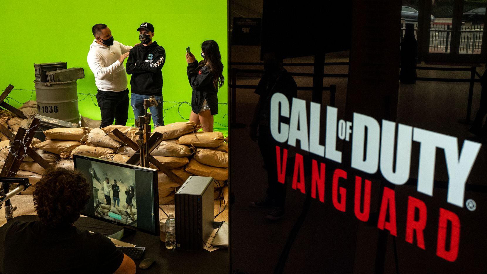 From left: Christian Bourdeax pretends to dust off Kevin Pichardo as Malee Mabandit takes a photo in a Call of Duty green screen booth to advertise the next game in the franchise, Call of Duty: Vanguard, on the final day of the Call of Duty league playoffs championship round on Aug. 22 at the Galen Center in Los Angeles.