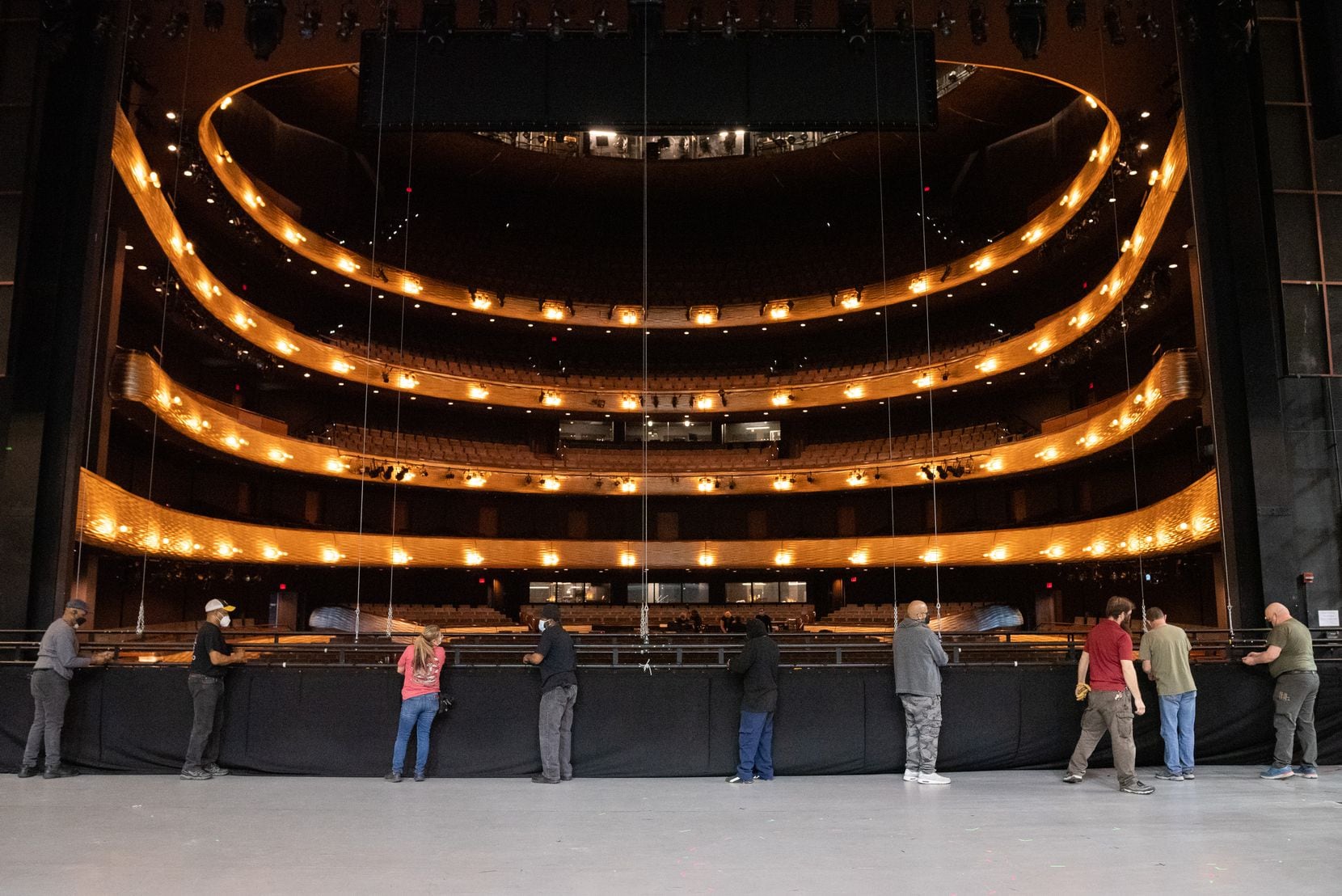 A group of stagehands works on installing the black show curtain during the set building for...