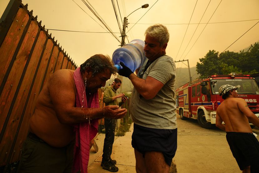 ARCHIVO - Un hombre ayuda a un vecino a refrescarse con una botella de agua mientras los...