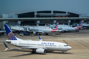 A United Airlines plane pushes away from a gate at Terminal E as American Airlines planes...