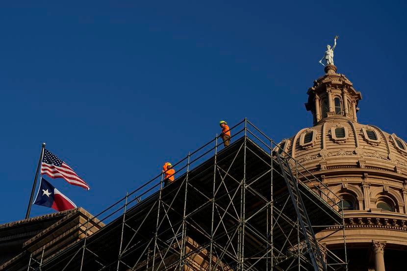 Construction workers look out from scaffolding for a roof restoration project as the Texas...