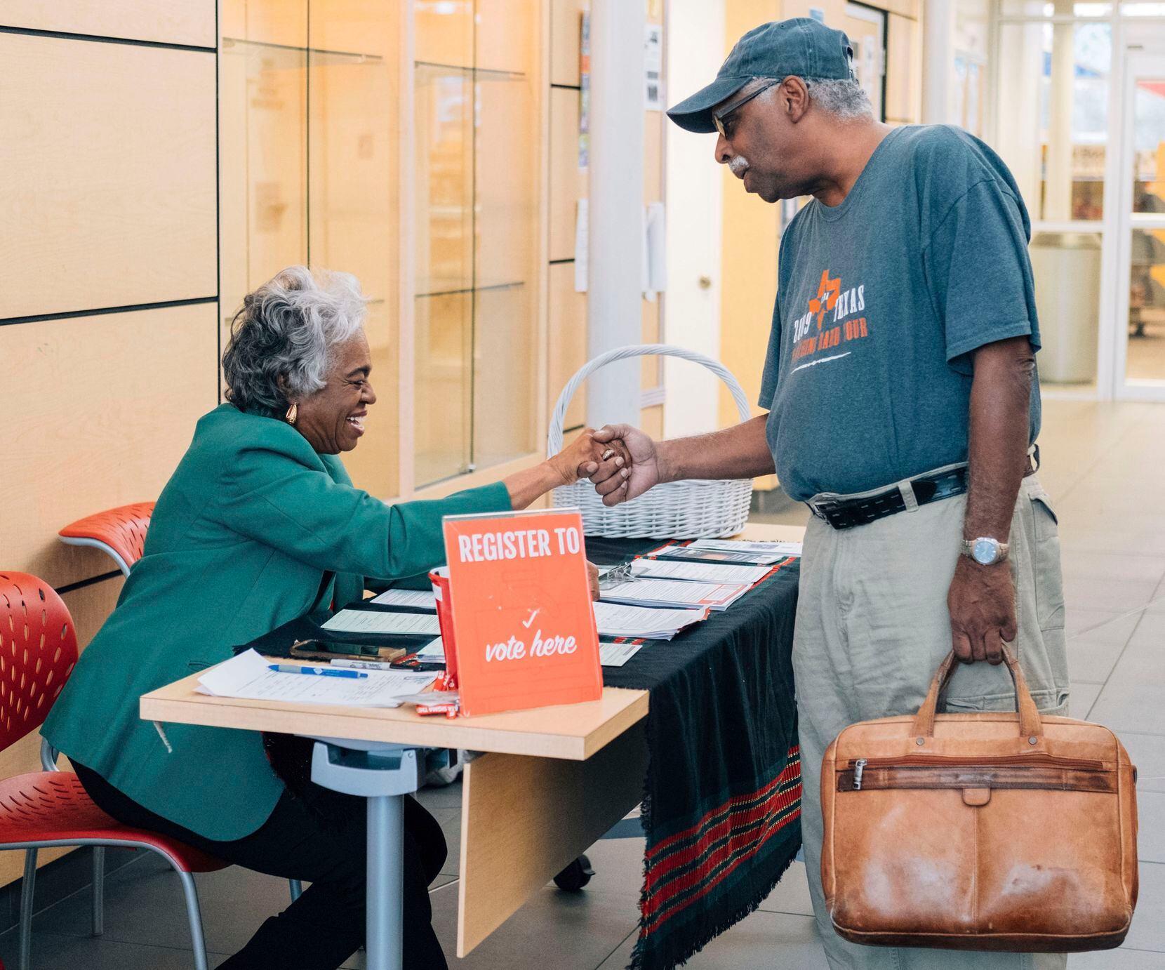 Sandra Malone shakes the hand of a Dallas resident at the Polk Wisdom Library as she registers people to vote, one of her volunteer gigs.