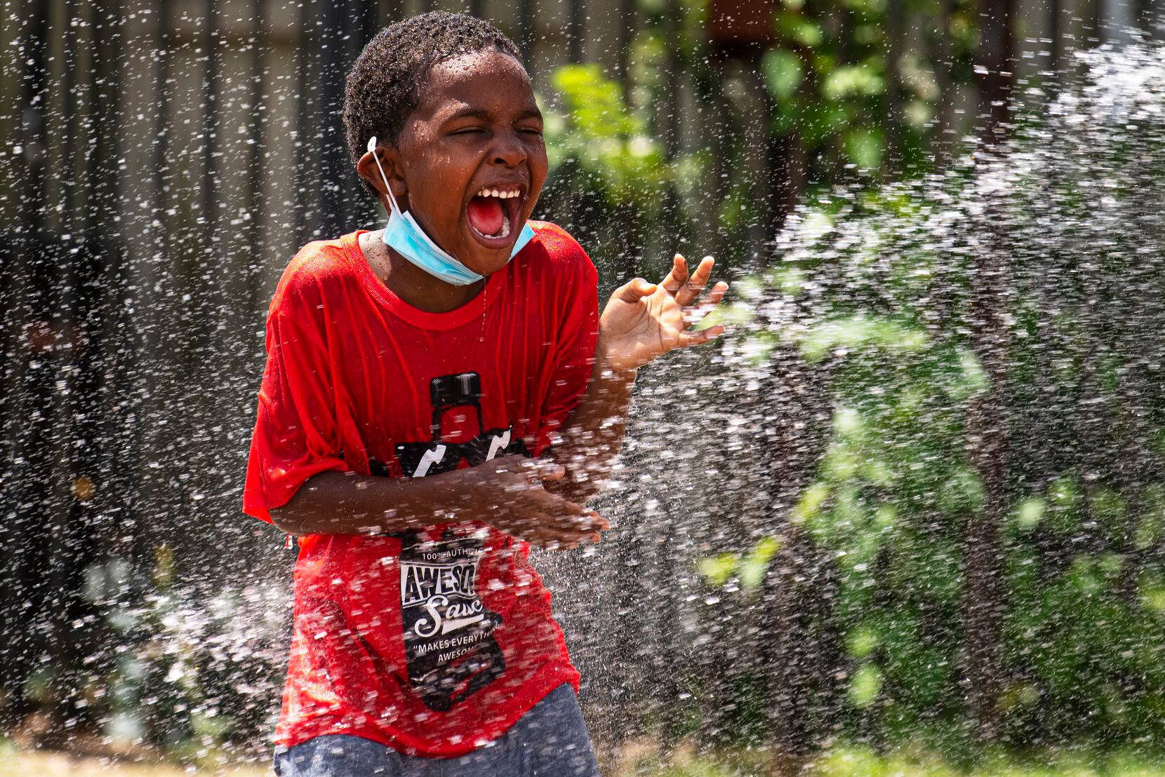 D'Erin Roland, 7, screams while being sprayed with water at the Frazier Revitalization...