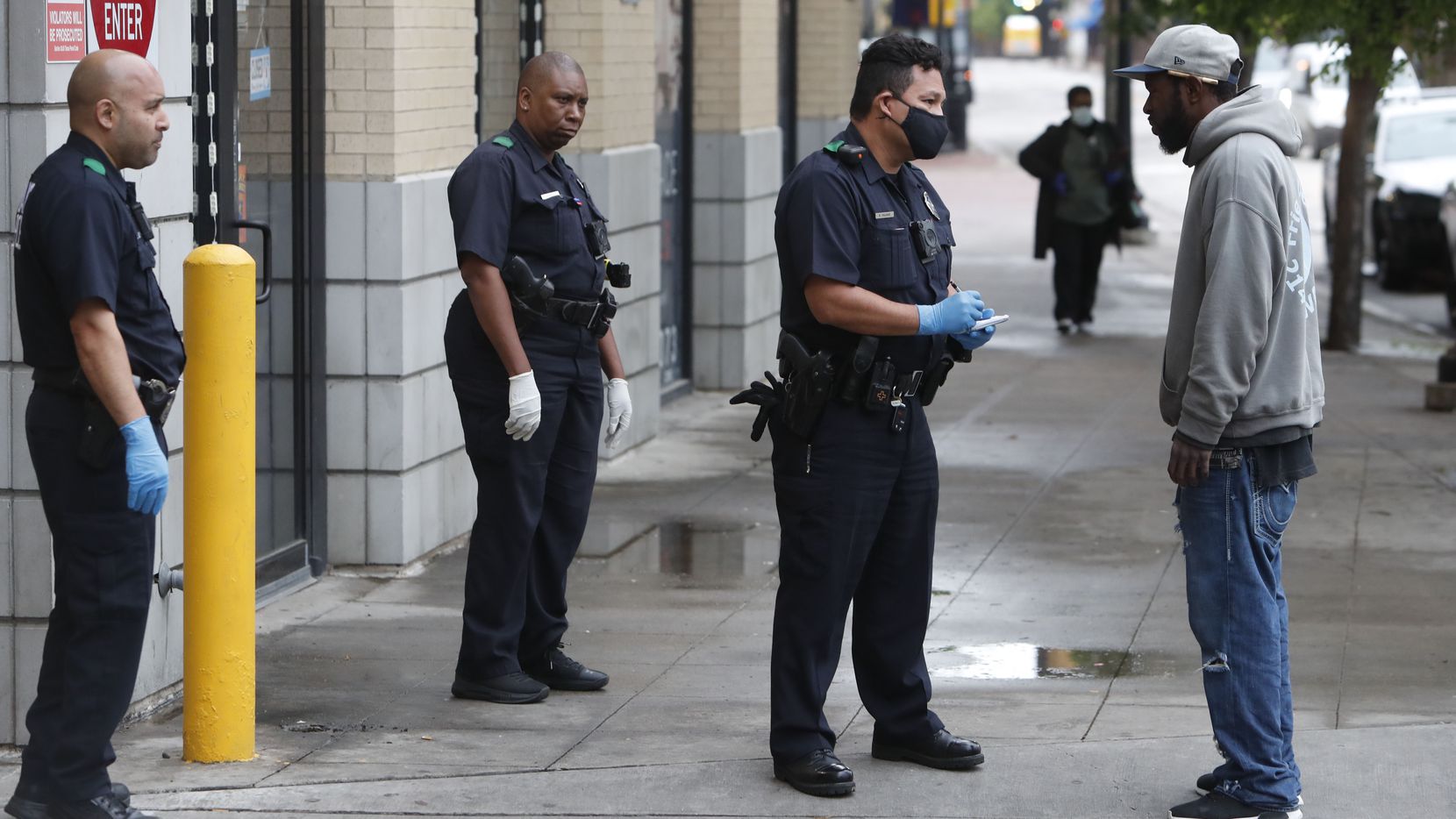 Practicing social distancing amid COVID-19 concerns, police officers speak with a man in...