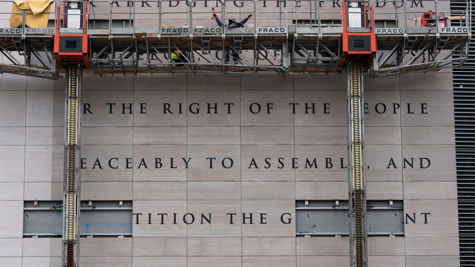 Workers remove a copy of the First Amendment from the front of the building that was...