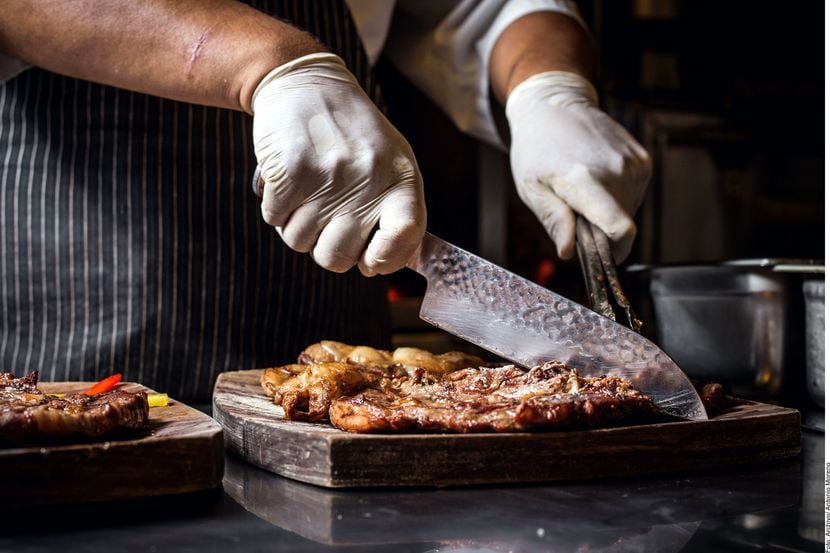 Foto de una persona cortando carne en una tabla de madera.