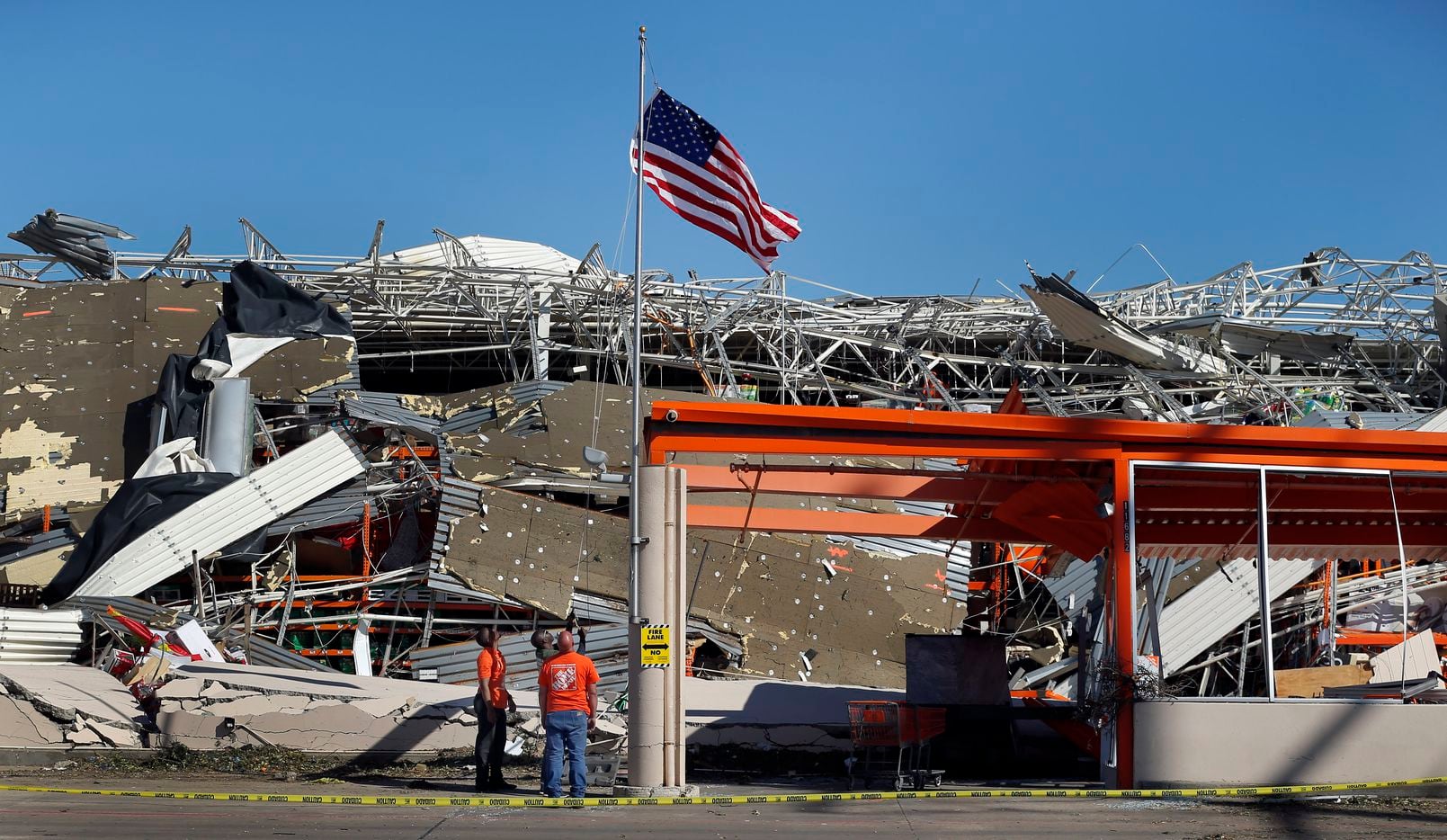 The Home Depot employees A.J. Kobena (center) raises the U.S. flag on the slightly bent flagpole outside the destroyed store on N. Central Expressway in Dallas, Monday, October 21, 2019. Jining him were fellow employees Jonathan Shields and Jordan Jasper. A tornado tore through the entire neighborhood knocking down trees and ripping roofs from homes.