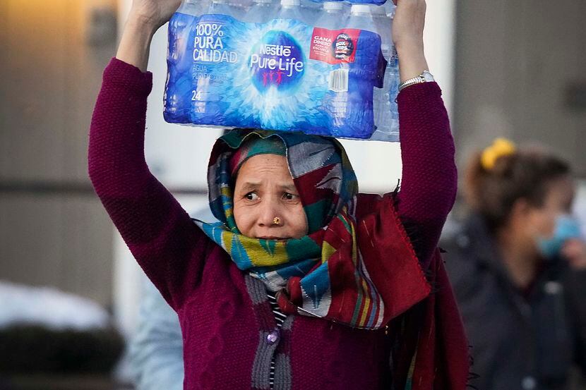 A woman carries two cases of drinking water distributed at the Literacy Achieves nonprofit...