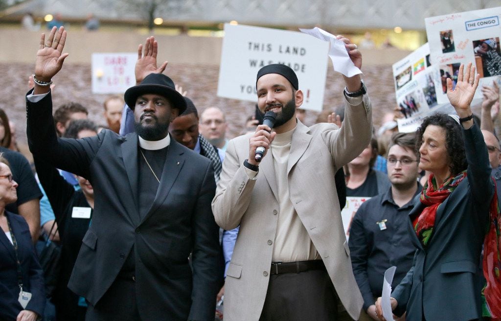 Iman Omar Suleiman, center, raises his hand with Rabbi Nancy Kasten, right, and the Rev....