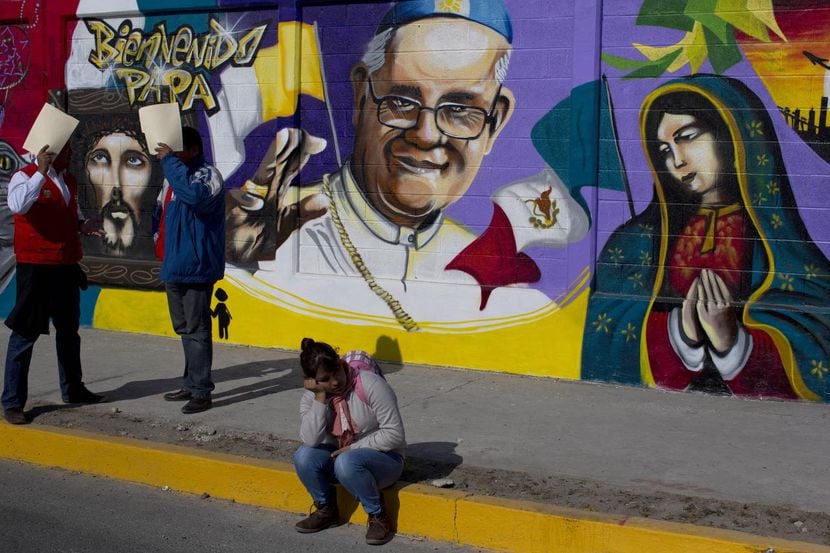 Una mujer se sienta frente a un mural con las imágenes del Papa Francisco y de la Virgen de...