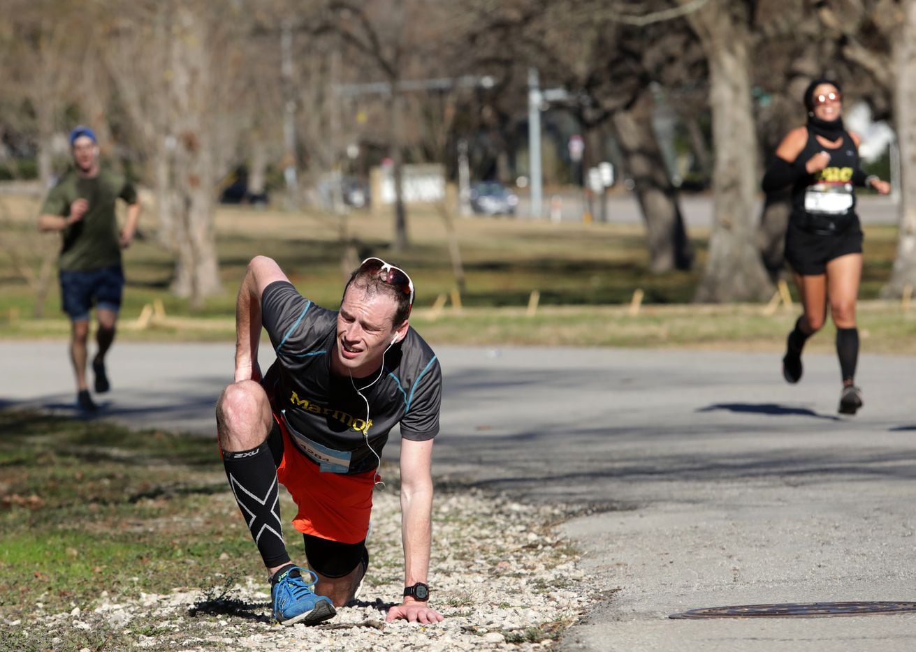 Seth Olson stretches to relieve a cramp during the BMW Dallas Marathon at White Rock Lake in...