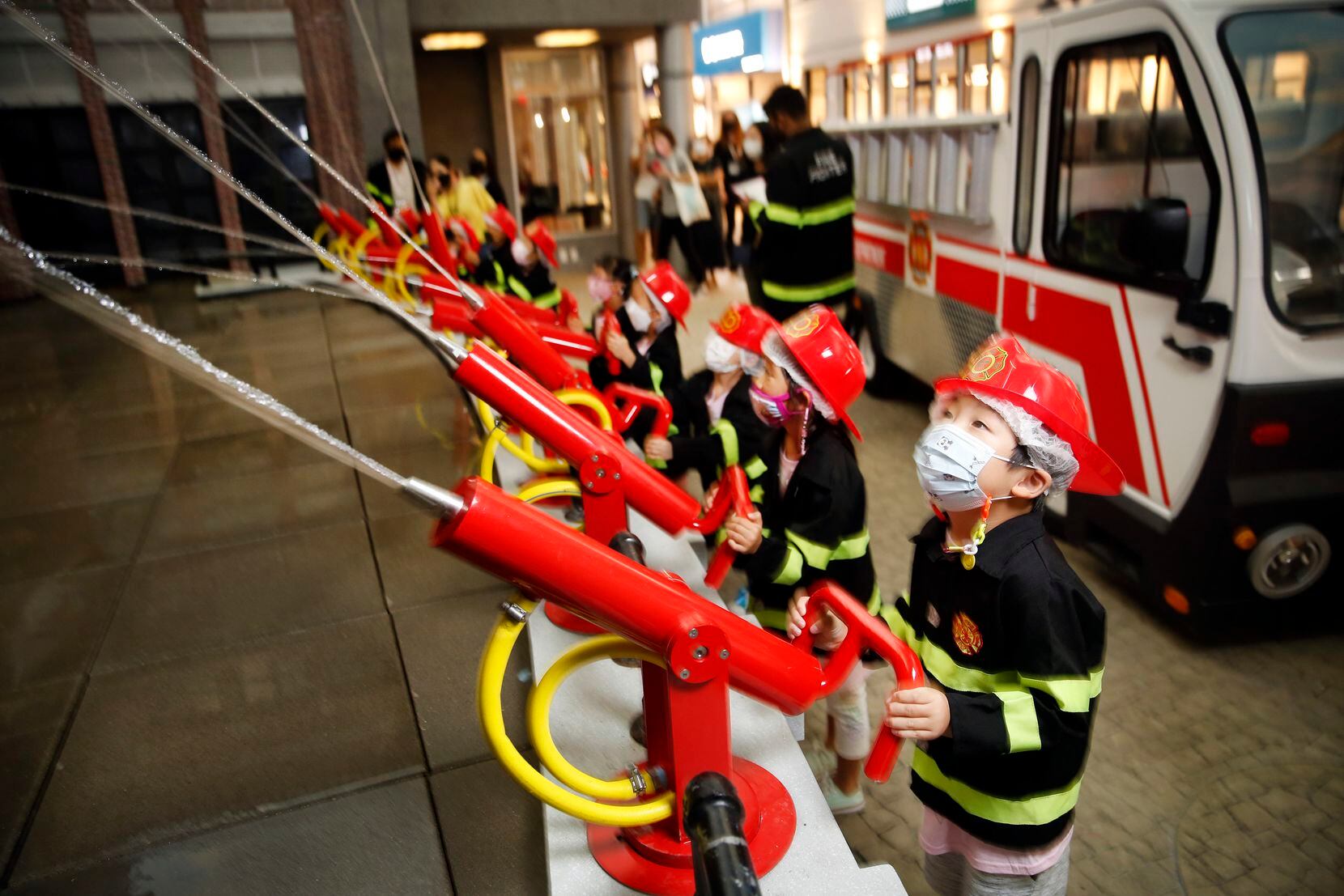Little ones dressed as firefighters spray water hoses on the 'burning' FlameZ match factory...