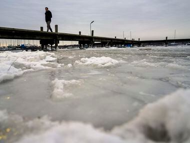 Frozen waters of White Rock Lake surround a pier after a winter storm brought snow and...