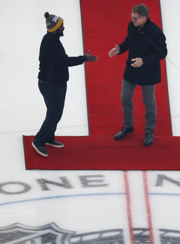 Troy Aikman, right, joins Ricky Williams, left, on the ice to participate in the puck drop...