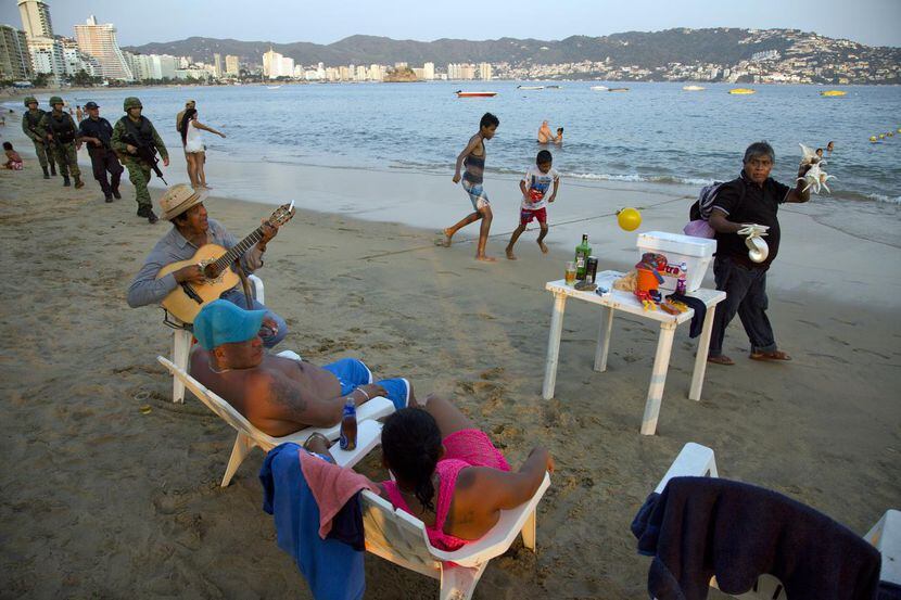 Soldados (izq.) patrulla la playa Papagayom en Acapulco, Guerrero, mientras una pareja...