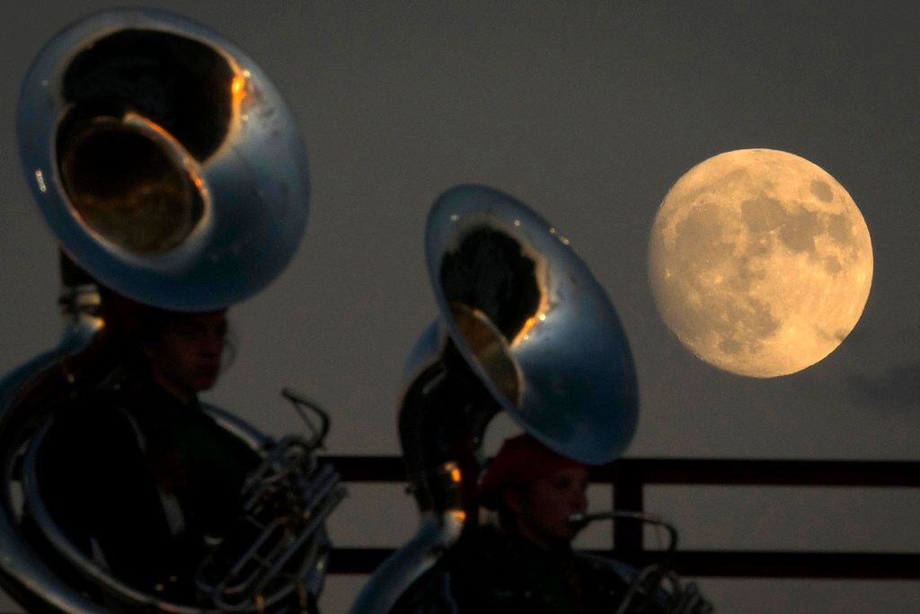 The moon rises over the Arlington High School band during a high school football game...