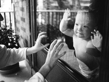 Separated by a window pane, a mother playfully taps on the glass while her child watches.