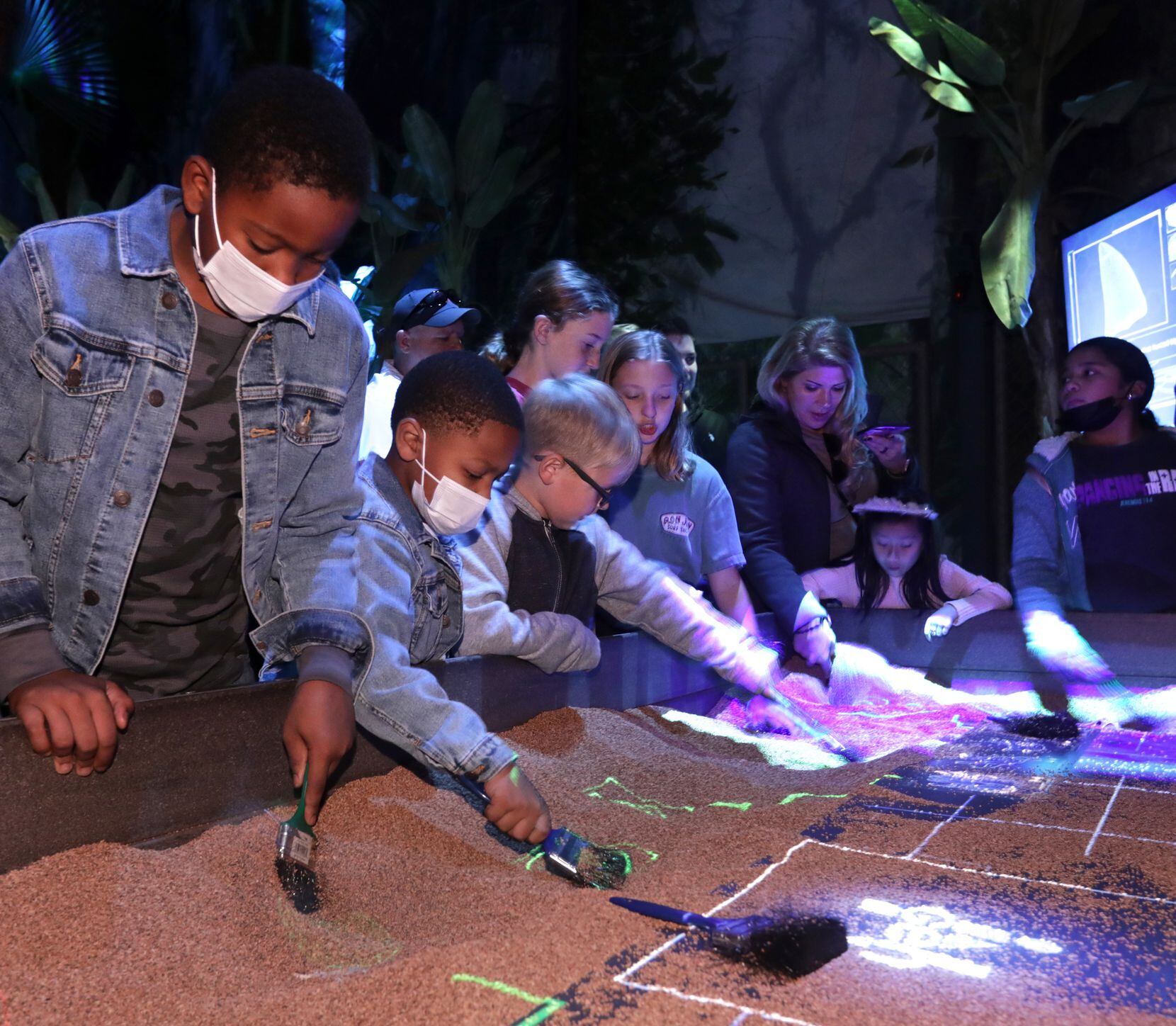 Guests brush away sand to find fossils at “Jurassic World: The Exhibition,” at Grandscape in...