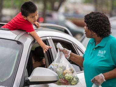 As he hangs out of his family’s car sunroof, Isaias Ovalle, 3, reaches for bagged school...