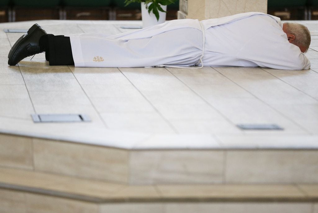 Bishop Edward J. Burns prostrates on the altar as a sign of humility and penance during a...