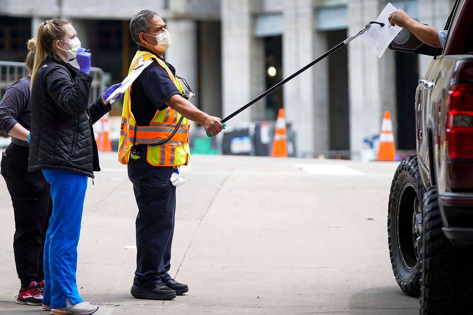 Healthcare workers use a pole to transfer paperwork to a person being tested at a COVID-19 drive-through testing site at American Airlines Center on Monday, April 20, 2020, in Dallas. Employment lawyers say the outbreak will allow companies to require their workers get testing, but legal liability remains in other areas. 