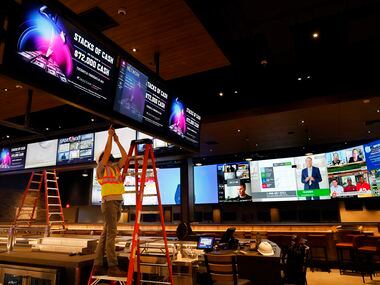 A worker puts the finishing touches on a bank of video screens hanging over The League...