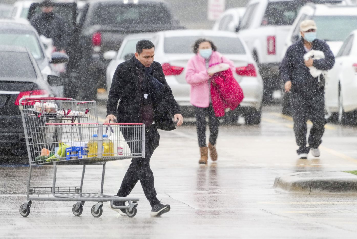 المتسوقون في متجر كوستكو في بلانو يتنقلون تحت المطر البارد بينما يتوجهون إلى سياراتهم في ...