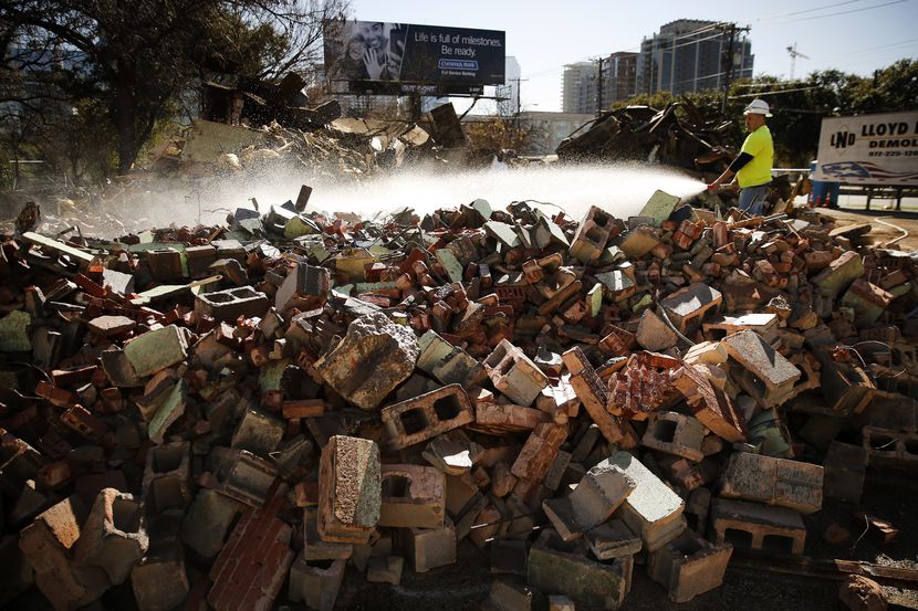 Demolition crewman Alex Robledo sprays water onto a pile of bricks that, until Tuesday, was...