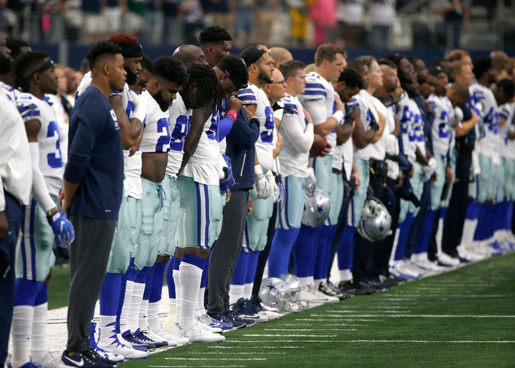 The Dallas Cowboys and staff stand on the sideline during the playing of the national anthem...