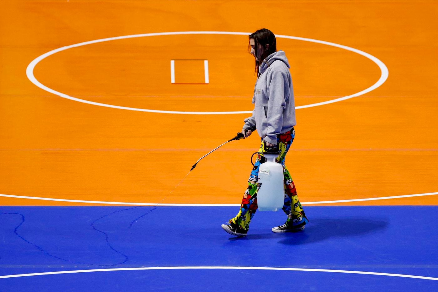 A person sprays a disinfectant on the mats during the UIL State Wrestling tournament at the...
