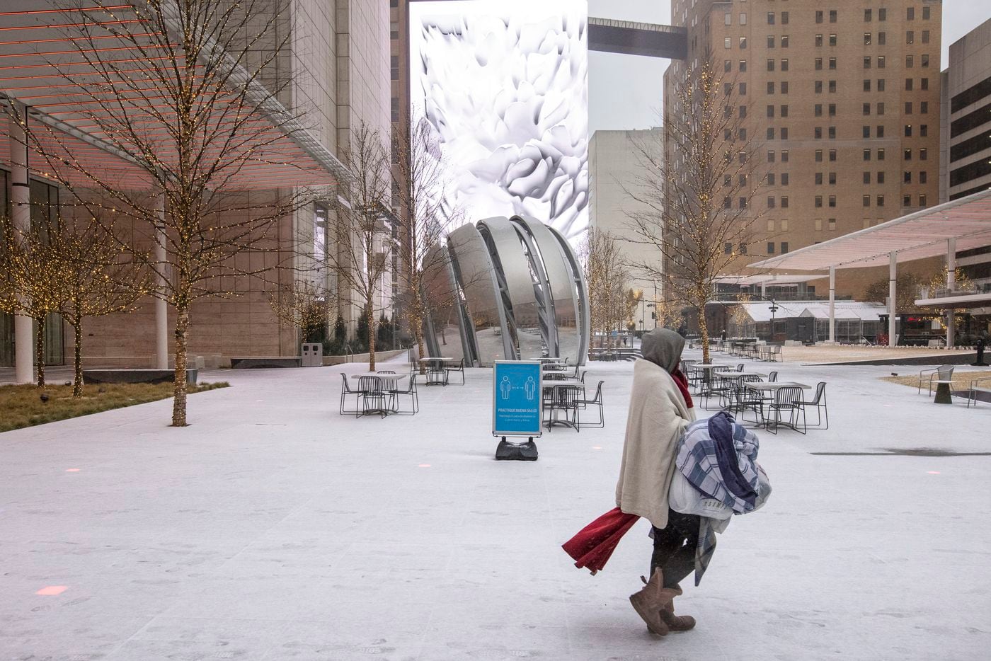 A person walks through snow past AT&T Discovery District in Downtown Dallas on Sunday, Feb. 14, 2021. The region is currently under a winter storm warning.