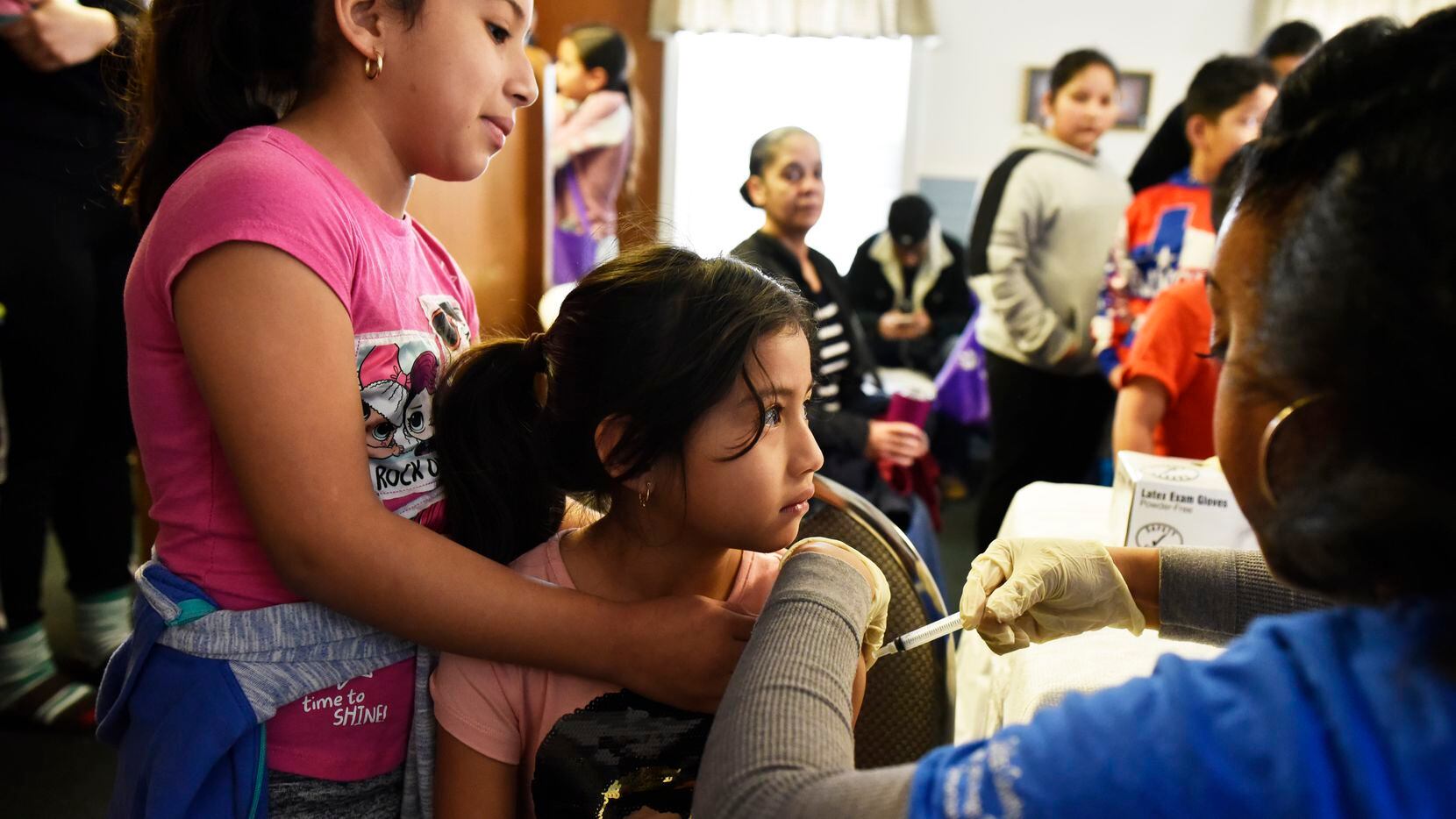 Kelin Rodriguez, 8, left, holds her sister Yennifer Rodriguez, 6, as she receives a flu...