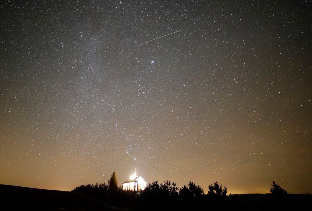 A meteor streaks across the sky during the annual Geminids meteor shower over an Orthodox...