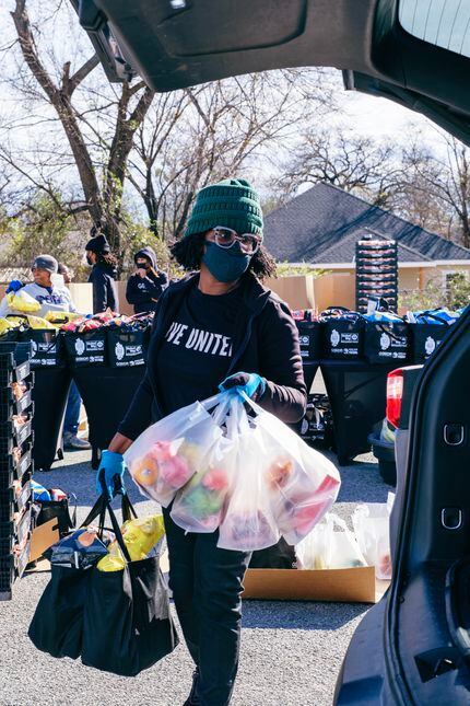 A Goodr volunteer wearing a mask and a "Live United" shirt carries grocery bags into the...