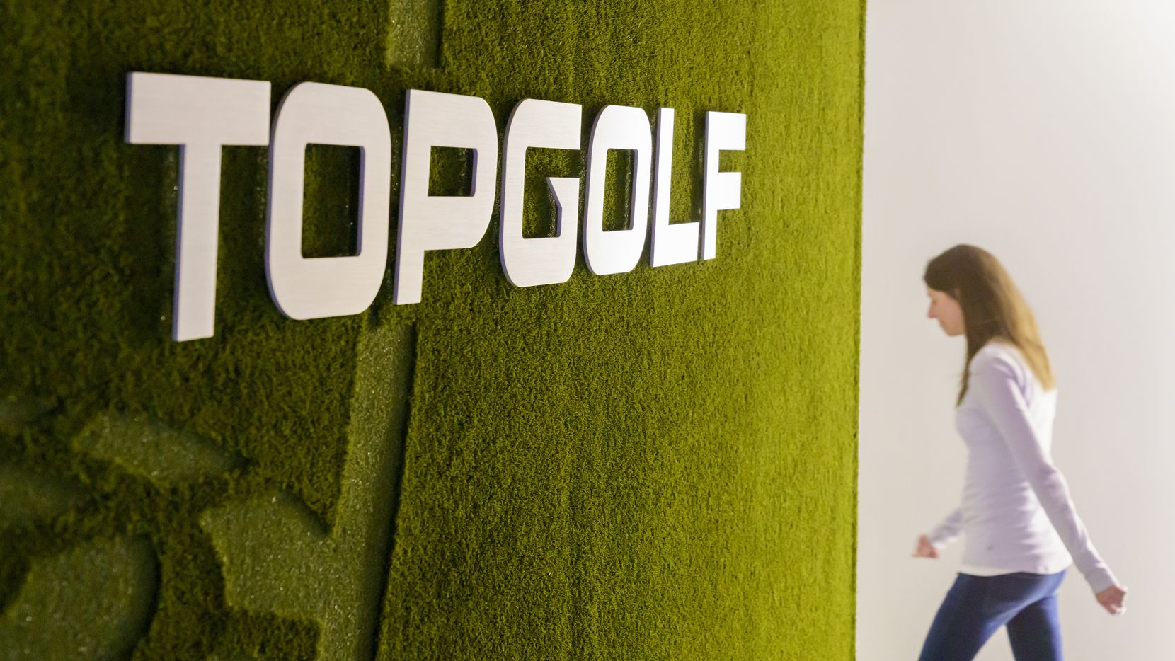 A wall covered in artificial turf and the company logo greets visitors in the lobby at Topgolf headquarters in 2019 in Dallas.