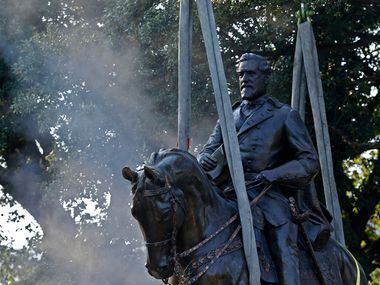 Workers cut the Robert E. Lee statue off of its base for its removal at Robert E. Lee Park...