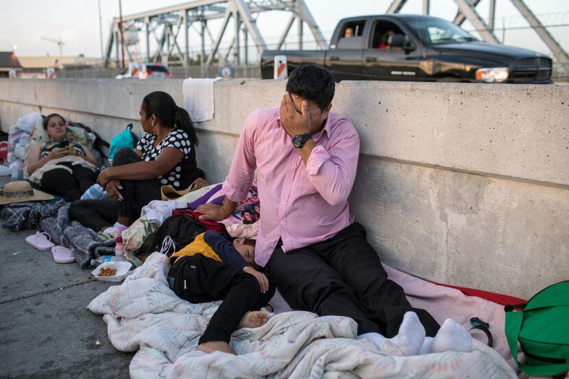 Un hombre hondureño y su hijo de 5 años esperan en el lado mexicano del Puente Internacional...