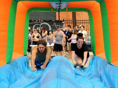 Friends slide down the slip 'n slide at the Deep Ellum Water Balloon Wars in Deep Ellum,...
