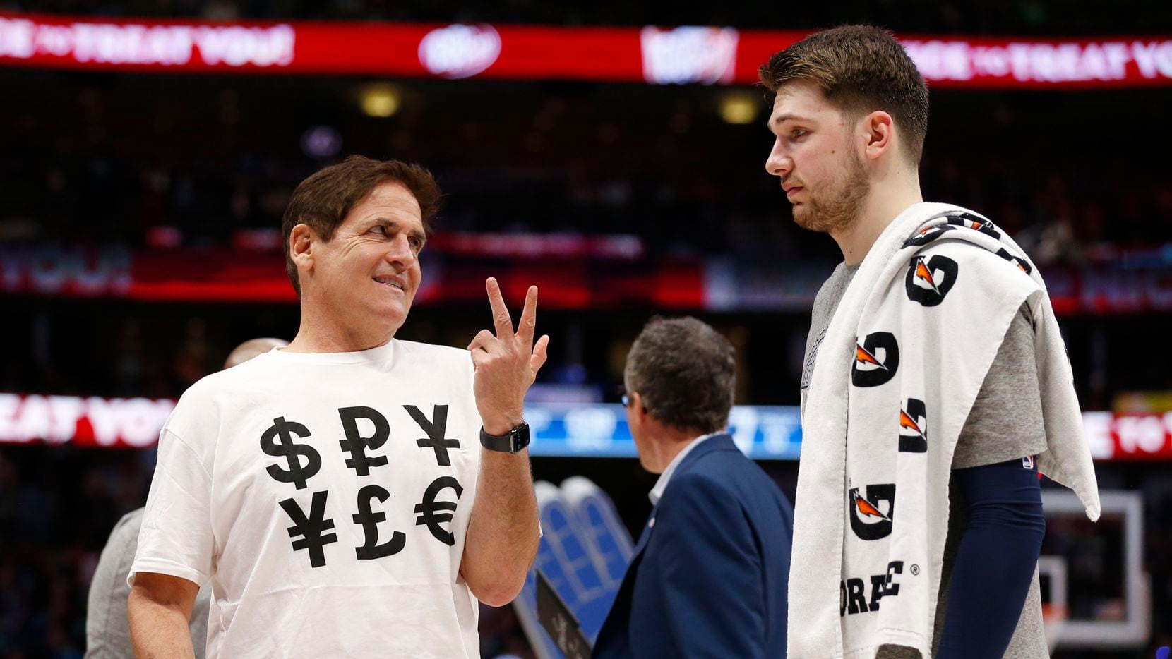 Dallas Mavericks owner Mark Cuban sports a shirt with money signs as he talks to Dallas Mavericks guard Luka Doncic (77) during the second half of play at American Airlines Center in Dallas on Friday, March 6, 2020. Dallas Mavericks defeated the Memphis Grizzlies 121-96.